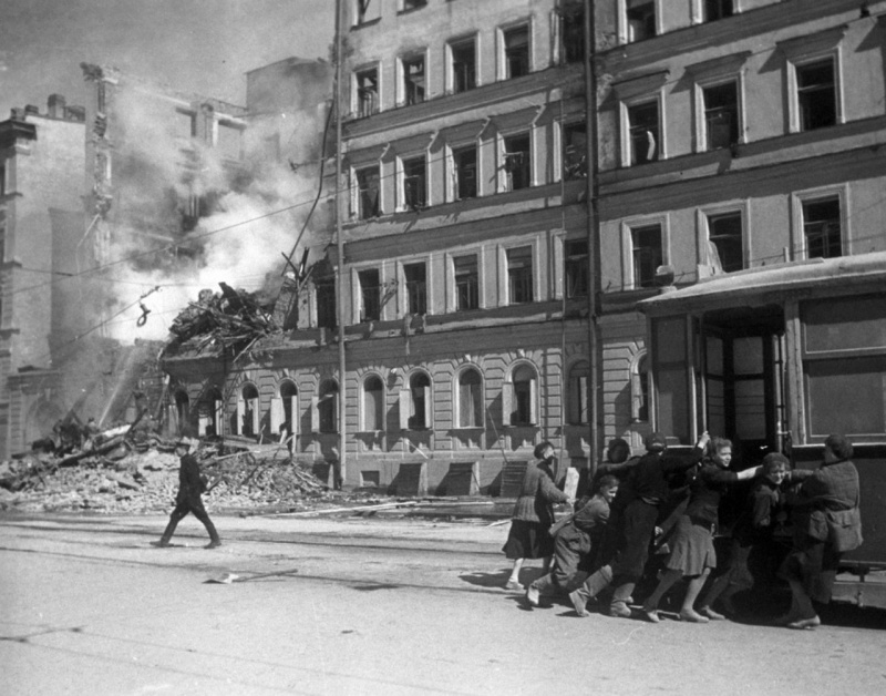 Жители блокадного Ленинграда передвигают трамвайный вагон подальше от фасада разрушенного бомбардировкой дома. 1942